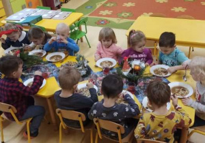 dzieci siedzą przy stole i jedzą obiad
