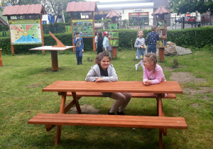 dzieci siedzą przy brązowym stoliku, który znajduje się na dworze